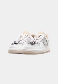 White leather sneakers with gray accents, textured finish, and beige tongue. Features round laces with tassels and a rubber sole.