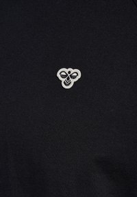 Mustast kangast, mille kesksele pinnale on tikitud väike valge mesilase logo.