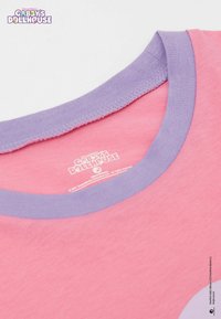 Růžové bavlněné tričko s lila žebrovaným kulatým výstřihem, na zadní straně má štítek s potiskem "Gabby's Dollhouse".