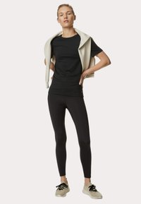 Camiseta negra ajustada combinada con leggings negros de cintura alta. Suéter beige claro caído sobre los hombros. Zapatillas con una suela texturizada.