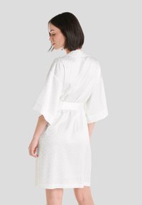 Bata estilo kimono blanca con mangas cortas, hecha de satén liviano. Cuenta con un cinturón atado y un sutil patrón tonal en la tela.