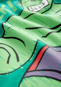 Grüner Stoff mit einer stilisierten Comicfigur in schwarzen Umrissen. Die Textur ist glatt mit lebendigen Farben und gewagtem grafischen Design.