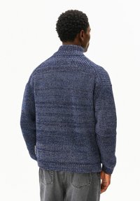 Marineblauer Strickpullover mit hohem Rollkragen, ausgestattet mit einem strukturierten Muster und gerippten Bündchen. Das Material zeigt eine Mischung aus dunklen und hellen Fäden.