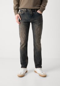 Jeans azul oscuro con un acabado desgastado, diseño de cinco bolsillos, acentos de costura y un corte recto, combinados con zapatillas blancas.
