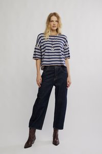 Črtast modro-bele barve širok vrh, kombiniran s temnimi kavbojkami širokih hlačnic in rjavimi gležnjarji. Ogrlica z okroglim obeskom.