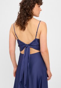 Granatowa satynowa sukienka z cienkimi ramiączkami, z tylnym wiązaniem i otwartym plecami, gładka struktura oraz zwiewny krój.