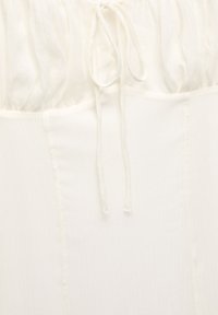 Top blanco hecho de una tela ligera y texturizada. Cuenta con un cordón en el escote y costuras verticales para dar forma. Acabado suave.