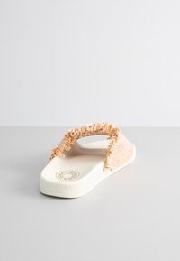 Light pink slip-on sandal with textured strap, featuring ruffled accents and a white textured sole, designed for comfort and casual wear.