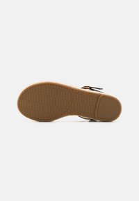 Suela de goma marrón con patrón texturizado y tacón redondeado. Presenta una correa negra con detalles de hardware dorado. Diseño plano en general.