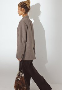 Blazer noir surdimensionné en tissu texturé, associé à un pantalon noir à jambes larges. Un sac à main avec un motif à pois est tenu.