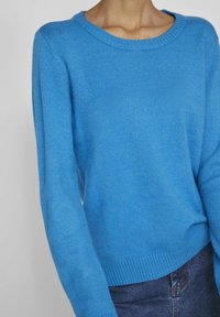 Pull tricoté bleu vif avec un col rond et des poignets et un bas côtelés. Le design présente une texture douce et une coupe décontractée.