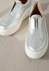 Stříbrné slip-on boty s robustní bílou platformou, s hladkým povrchem a elastickými postranními panely pro snadné obouvání.