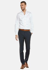 Weißes Hemd mit Knöpfen, marineblaue Hose, brauer Leder-Gürtel und Schuhe. Das Hemd hat lange Ärmel; die Hose ist eng geschnitten. Einfaches, klassisches Outfit.