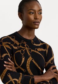 Pulover negru din tricot cu un model de lanț auriu, guler rotund și mâneci lungi, cu o textură moale și o siluetă ajustată.