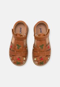 Lædersandaler med en brun nuance, der har vævede stropper og broderede jordbær og blomster. Velcro-lukning for nem påtagning.