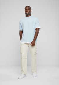 T-shirt bleu clair à manches courtes, avec des accents blancs aux manches, associé à un pantalon cargo beige comportant plusieurs poches et une coupe décontractée.