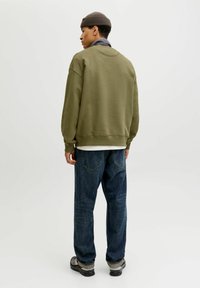 Oversized sweatshirt w kolorze oliwkowym z prążkowanymi mankietami i dołem, w zestawieniu z ciemnoniebieskimi dżinsami o prostym kroju oraz szarymi sneakersami.