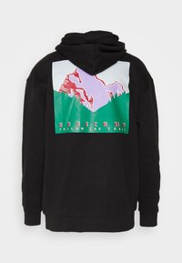 Sudadera con capucha negra con un gráfico de una montaña púrpura y roja sobre un bosque verde, con el texto "BASE CAMP FOLLOW THE TRAIL" en la parte trasera.