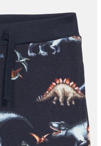 Σκούρο μπλε ύφασμα με πολύχρωμες απεικονίσεις δεινοσαύρων και ιπτάμενων ερπετών, με ριμπ ζώνη μέσης και λεπτομέρεια κορδονιού.