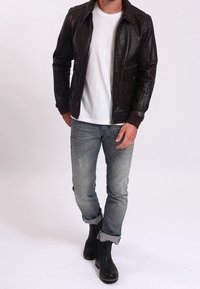 Hnědá kožená bomber bunda se zipem vpředu, špičatým límcem a bočními kapsami; doplněná světle modrými roztrhanými džínami a černými kotníkovými botami.