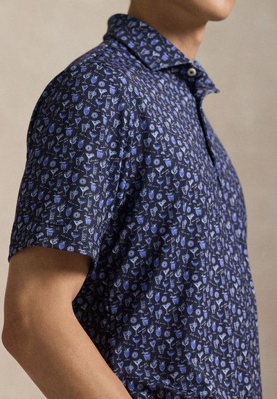 Κοντομάνικη πόλο μπλούζα σε σκούρο ναυτικό μπλε, με επαναλαμβανόμενο σχέδιο από ποτά και φέτες εσπεριδοειδών. Μαλακό ύφασμα με γιακά και κλείσιμο με κουμπιά.