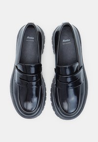 Mocasines de cuero negro con un acabado brillante, presentan una correa en el empeine, suela de goma gruesa y logotipo grabado en el interior.