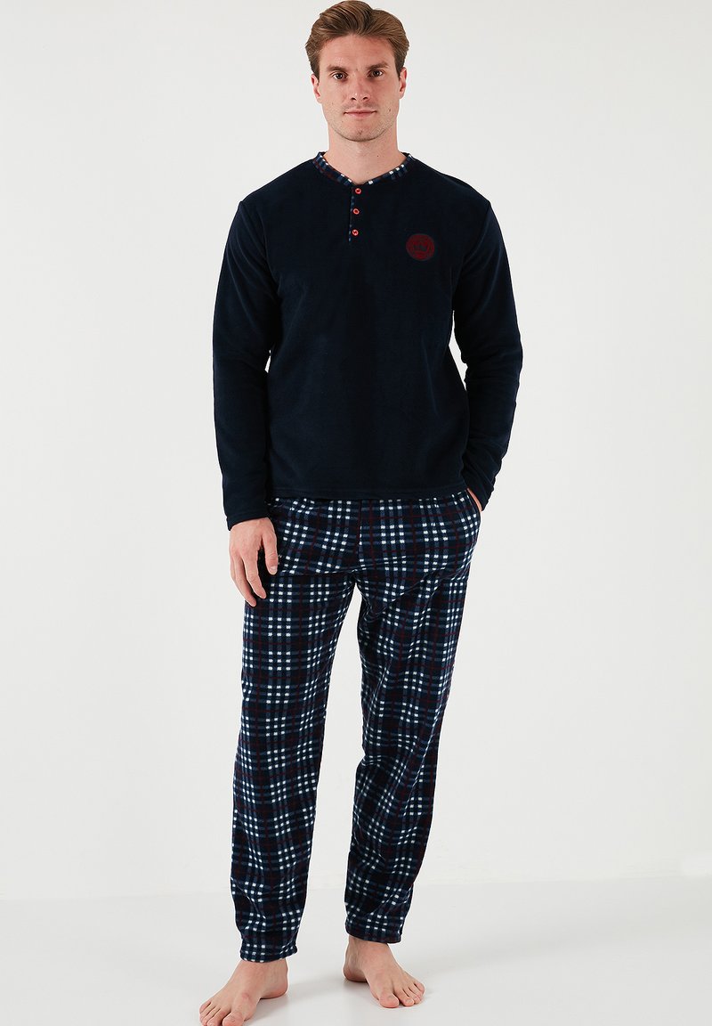 Herrepyjamas med en marineblå fleece-overdel med henley-krave og knapdetaljer, parret med bukser i mørke nuancer med ternet mønster.