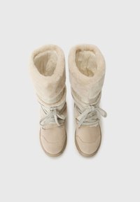 Beige téli csizmák bolyhos béléssel, fűzőkkel és lehajtható szárú kivitelben. A háttér sima fehér.