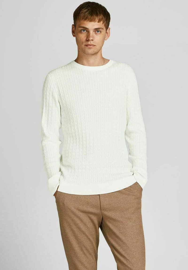 Maglione a maglia rigata, con scollo rotondo in un leggero avorio, caratterizzato da maniche lunghe e una vestibilità rilassata, abbinato a pantaloni marroni su misura.