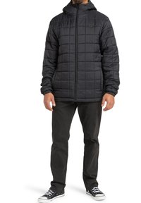 Giubbotto imbottito nero con cappuccio, cerniera frontale e polsini elasticizzati. Indossato sopra pantaloni scuri e sneakers nere.