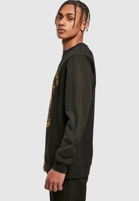 Czarny sweter z prążkowanymi mankietami i dekoltem, z kolorowym nadrukiem na przodzie. Gładka tekstura, luźny krój.