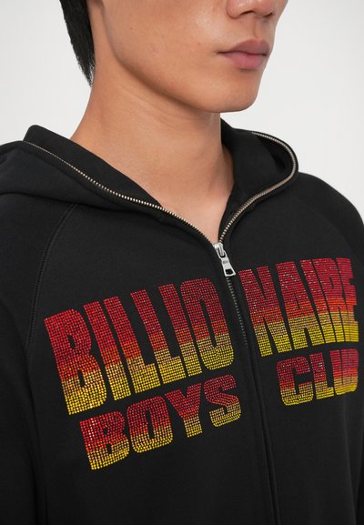 Crna zip-up dukserica s odvažnim natpisom "BILLIONAIRE BOYS CLUB" u gradijentu od crvene do žute. Mekana tkanina s teksturiranim završetkom.