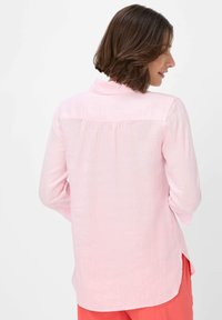Light pink shirt with long sleeves, collar, and back pleat detail. Made of soft fabric, featuring a curved hem and side slits.