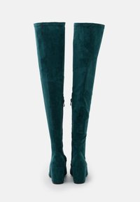 Bottes montantes bleu sarcelle en daim doux, au design ajusté, talons carrés et détails de laçage sur le côté pour un ajustement réglable.