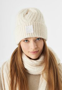 Gebreide crèmekleurige beanie met een ribdesign en een getextureerde vierkante patch. Draagt u met een bijpassende crèmekleurige sjaal voor een gecoördineerde uitstraling.
