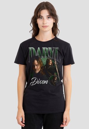 Young woman wearing black T-shirt with green and white "Daryl Dixon" text and three character images holding a crossbow from a TV series.