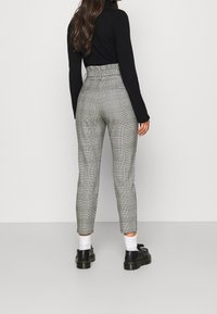 Gray plaid trousers with a high waist and tapered fit, featuring a textured fabric and contrasting black accents at the shoes.