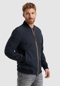 Cazadora bomber de la marina hecha de un tejido ligero, con una cremallera dorada, puños acanalados y bolsillos laterales para un diseño elegante.