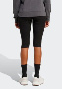 Črne legice do kolen, kombinirane z belimi športnimi čevlji in črnimi nogavicami, nošene s sivo jopa. Oblikovanje iz gladkega, raztegljivega blaga.