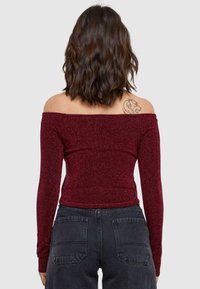 Burgundy, váll nélküli felső hosszú ujjal, csillogó anyagból készül, testhez simuló fazon, sötét, magas derekú farmerral párosítva.