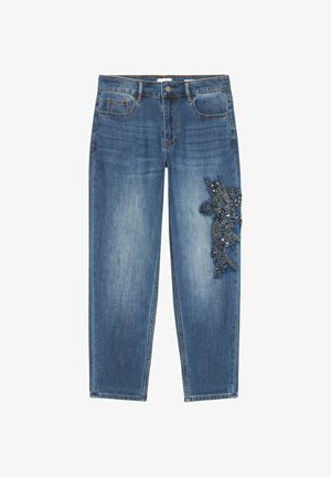 Vaqueros de mezclilla azul con cintura alta y cierre de botones, que presentan un detallado adorno floral de cuentas oscuras en el muslo derecho.