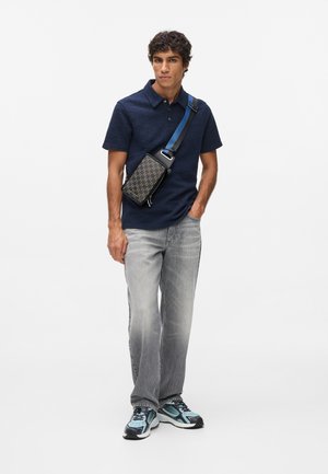 Tumes tekstuuriga polo särk, hallid teksad ja mustriga õlariba kott sinise sangaga. Mustad ja sinised spordijalatsid lõpetavad komplekti.