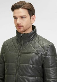 Giacca in pelle verde trapuntata con collo alto e zip frontale. Presenta motivi orizzontali e a rombo, una consistenza morbida e un design elegante.
