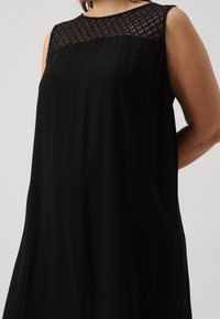 Svart ärmlös klänning med en texturerad spetskrage, flödande tyg och avslappnad passform. Slät textur med en elegant silhuett.