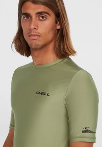 Rash guard s kratkimi rokavi v olivno zeleni barvi, izdelan iz lahkega, raztegljivega materiala, vključuje O'Neill blagovno znamko in UV zaščitne podrobnosti na rokavu.
