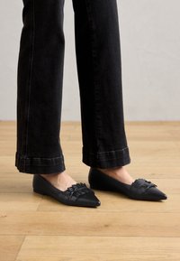 Sorte flate sko med spiss tå, med en teksturert vevd overdel og dekorativ sløyfe. Brukt sammen med svarte cropped jeans.