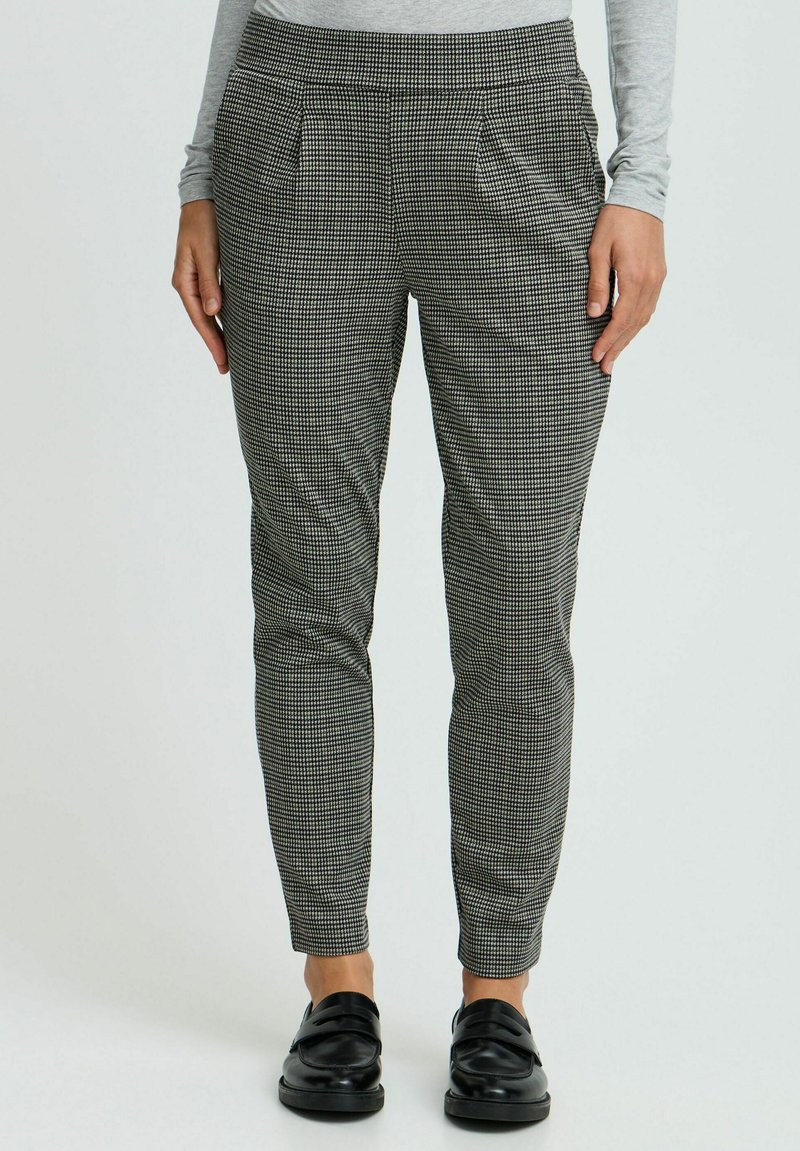 Black and white checkered trousers with pleated front, tapered fit, and elastic waistband, paired with black leather loafers.