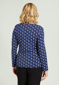 Top met lange mouwen met een geometrisch patroon in blauw, zwart en wit, gemaakt van een soepele stof en een ronde halslijn. Zwarte broek niet inbegrepen.