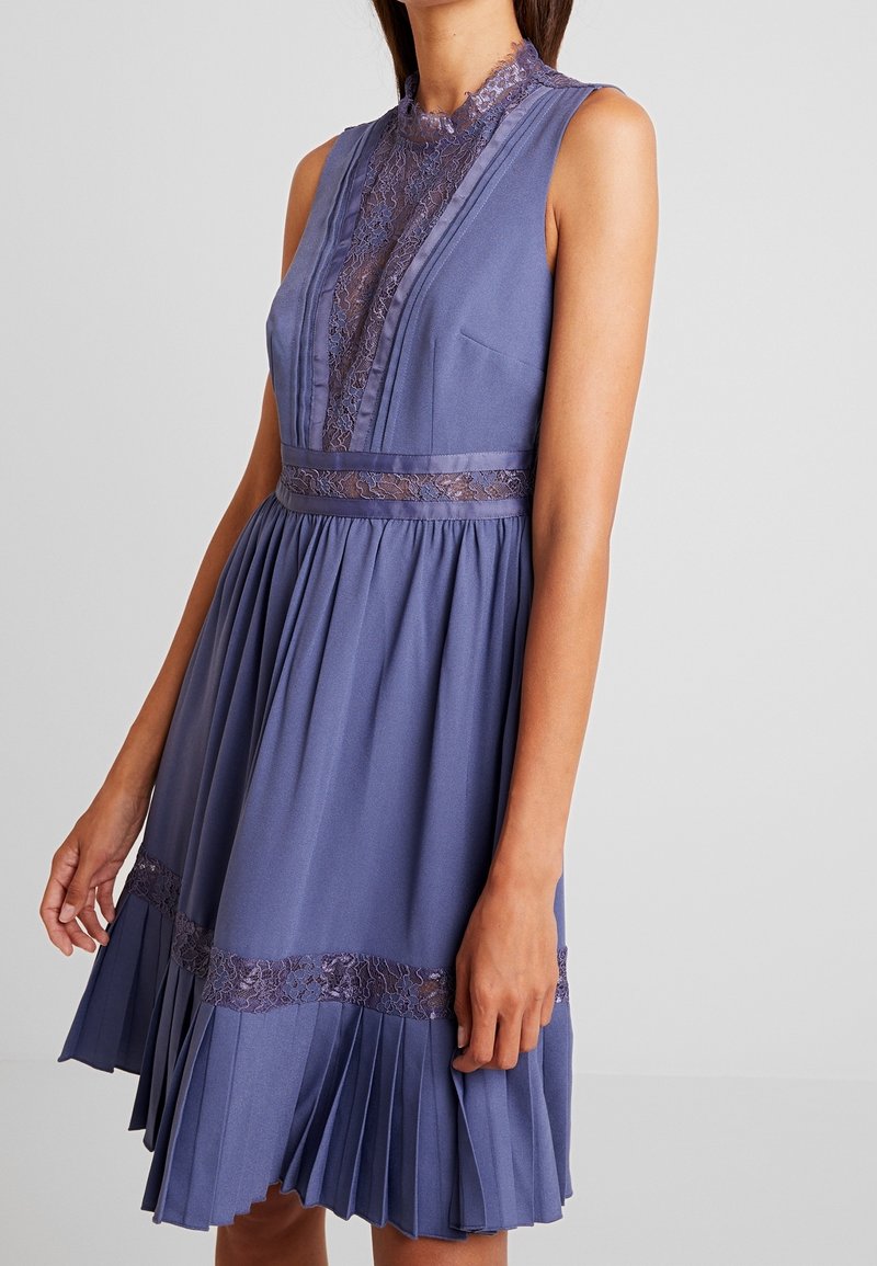 Hihaton violetti mekko, jossa pitsiyksityiskohtia kaula-aukossa ja vyötäröllä. Pliseerattu hame, jossa pitsikoristeita helmassa, kevyt kangas.
