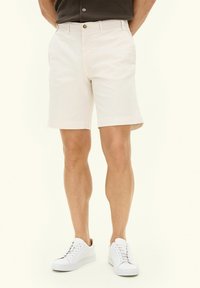Pantaloni short chiari in cotone, con chiusura a bottone, tasche laterali e taglio dritto, abbinati a sneakers bianche.